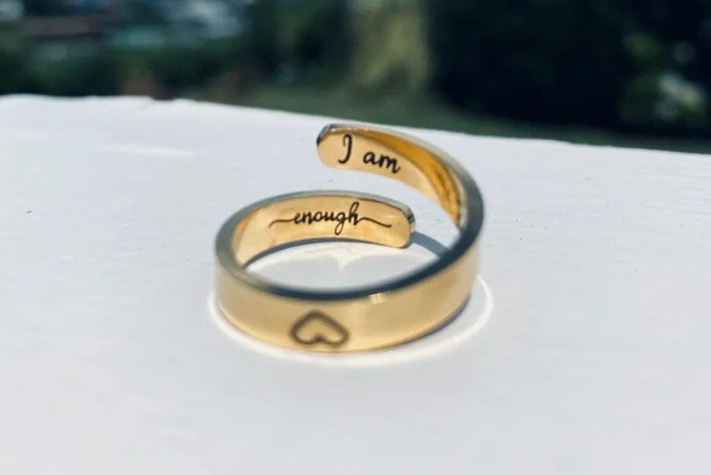 Gold ring with engraved text on a white surface with a blurred natural background